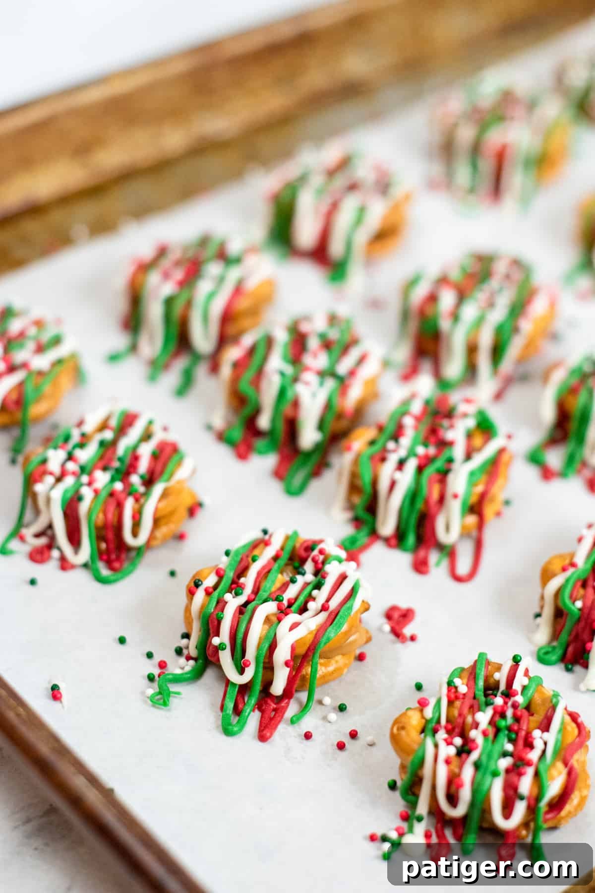 Holiday Pretzel Poppers 7 Christmas Pretzel Bites on a parchment-lined baking sheet, topped with red, green, and white candy drizzles and festive Christmas sprinkles.