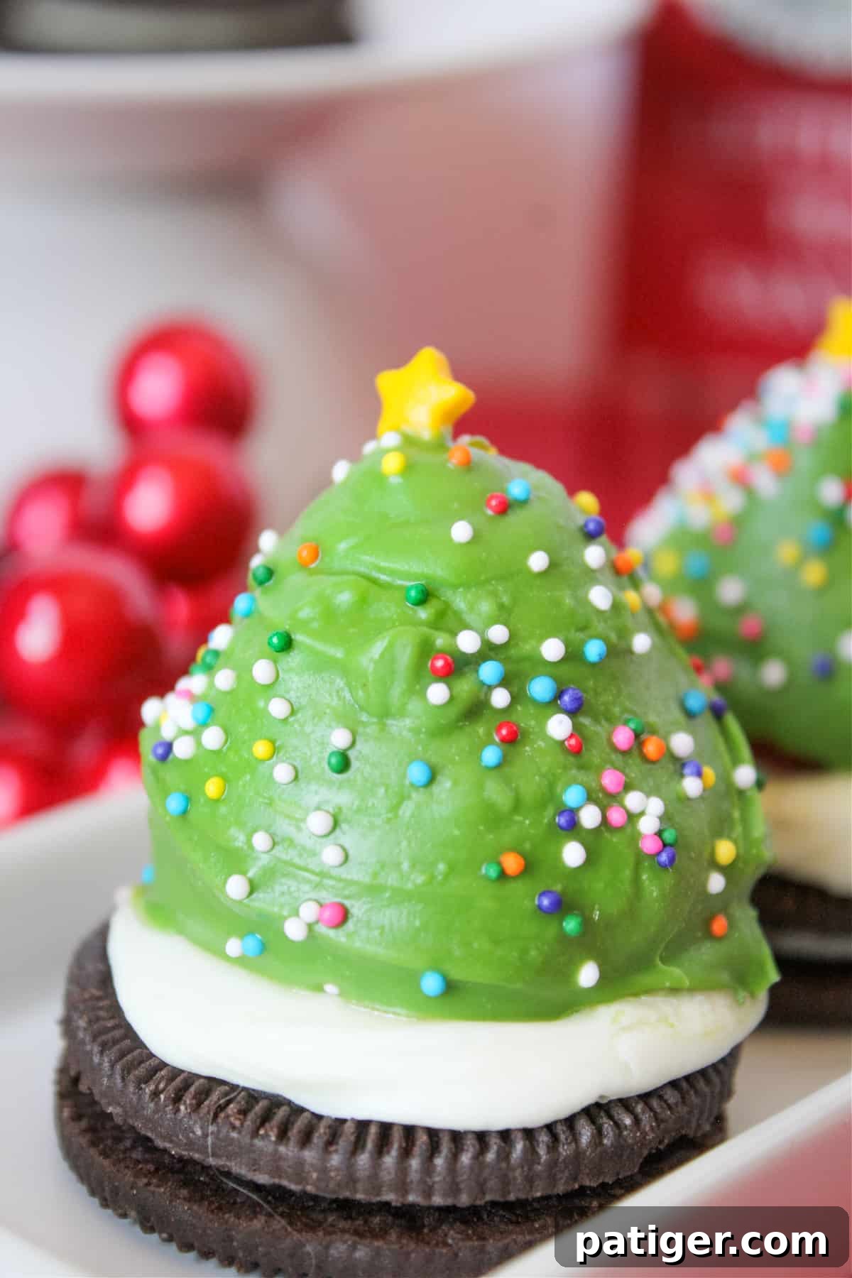 Strawberry dipped in green chocolate and decorated with sprinkles to look like a Christmas tree. The berry is sitting on an oreo cookie topped with vanilla frosting.