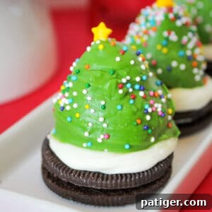 Strawberry dipped in green chocolate and decorated with sprinkles to look like a Christmas tree. The berry is sitting on an oreo cookie topped with vanilla frosting.