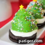 Strawberry dipped in green chocolate and decorated with sprinkles to look like a Christmas tree. The berry is sitting on an oreo cookie topped with vanilla frosting.
