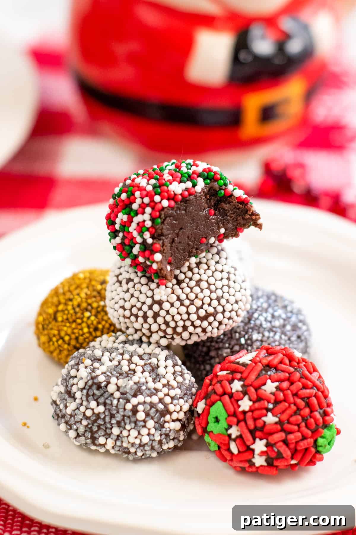 no-bake brownie batter truffles decorated with holiday sprinkles on white plate. On right, brownie truffles stacked on top of one another with a bite taken out of top one to show fudgy inside