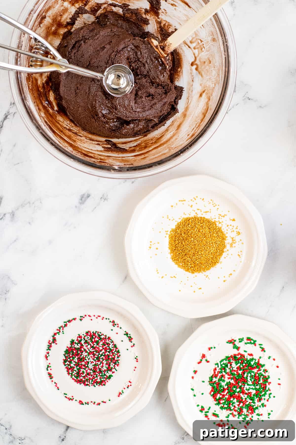 bowl of no-bake brownie batter with cookie scoop in it and three shallow bowls of different color sprinkles.
