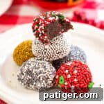 no-bake brownie batter truffles decorated with holiday sprinkles on white plate. On right, brownie truffles stacked on top of one another with a bite taken out of top one to show fudgy inside