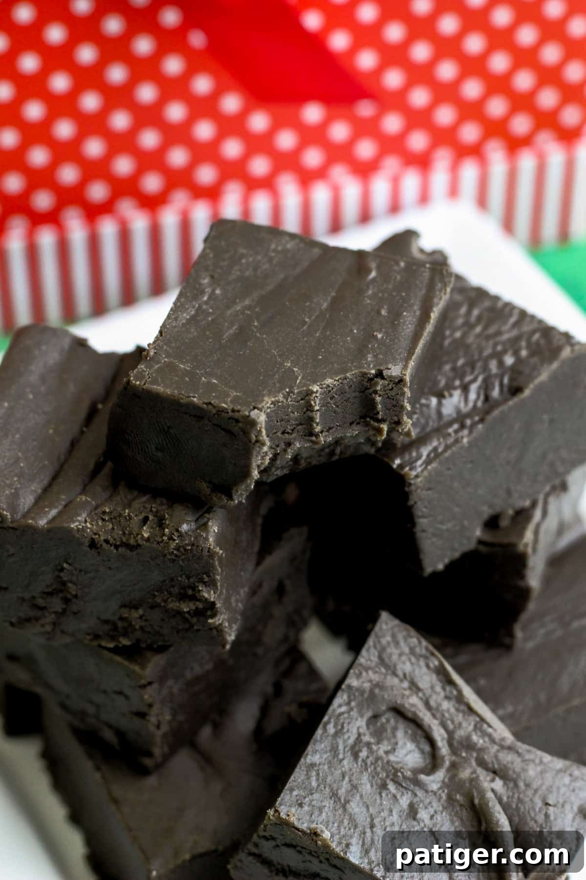 Pieces of black fudge stacked on white platter with christmas decor in background.