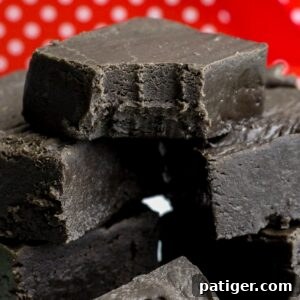 Black fudge cut in squares and stacked in a pile. The top piece has a bite taken out of it.