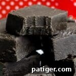 Black fudge cut in squares and stacked in a pile. The top piece has a bite taken out of it.