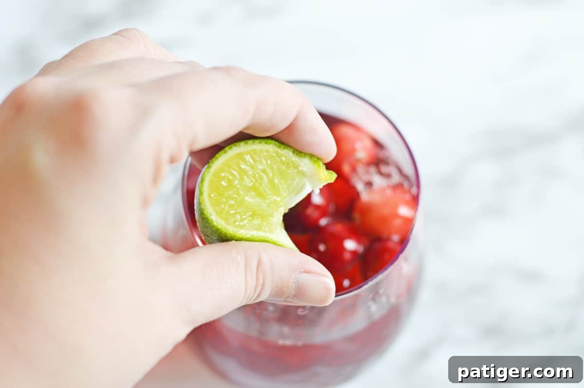 A hand expertly squeezing a fresh lime wedge into a Vodka Cranberry cocktail, highlighting the crucial step of adding citrus for balance.