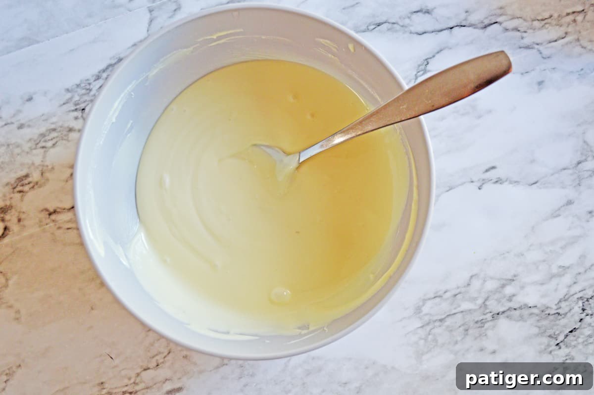 Smooth, glossy white melted candy in a clear glass bowl, perfectly prepared for the first layer of Grinch Bark.