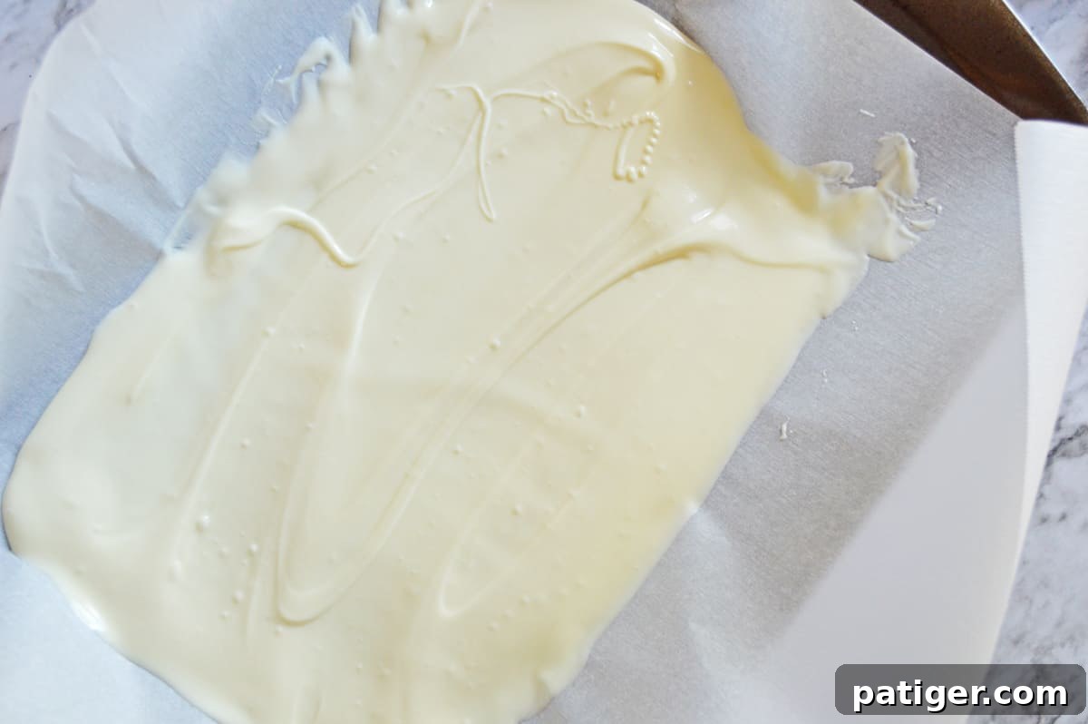 Melted white candy smoothly spread into an even, thin layer on a parchment-lined baking sheet, forming the base for the Grinch Bark.