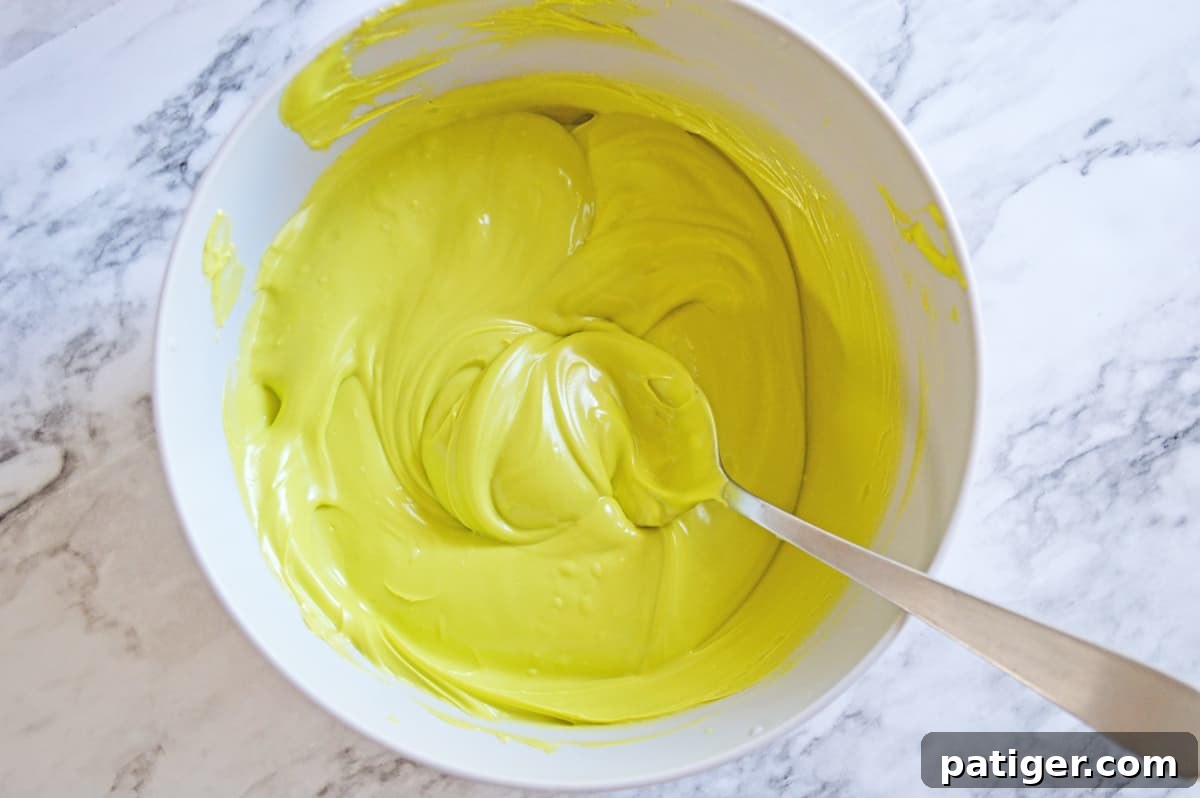 Vibrant green melted candy in a clear glass bowl, perfectly smooth and ready to be layered for the festive Grinch Bark.
