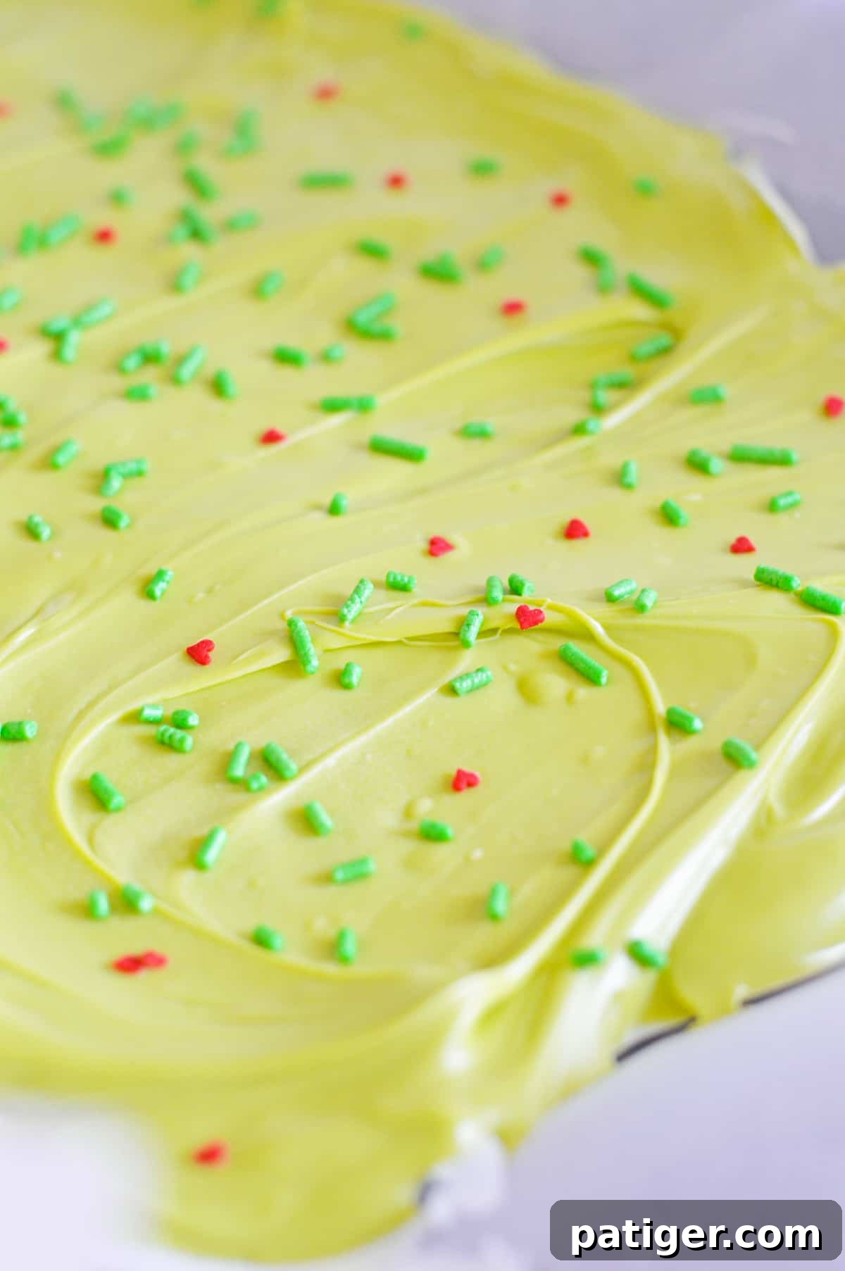 Fully set Grinch Bark, a vibrant green and white masterpiece with red hearts and green sprinkles, resting on a parchment-lined baking sheet, ready to be broken into pieces.