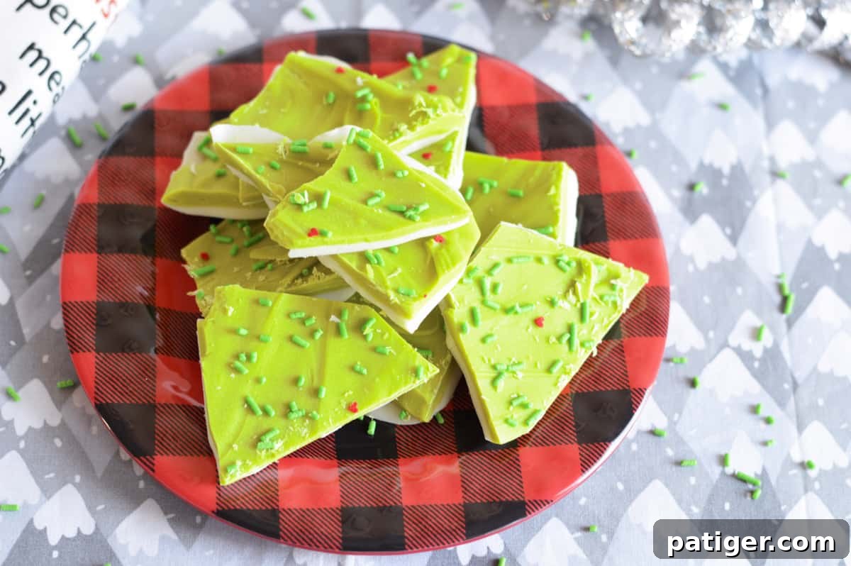 Delicious Grinch-themed bark candy, featuring green and white layers with red hearts, artfully arranged on a festive buffalo plaid plate, perfect for holiday snacking.
