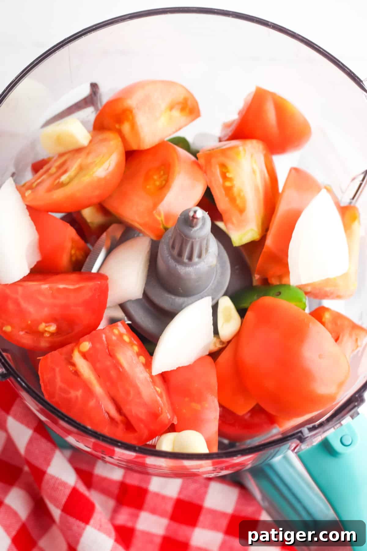 Roughly chopped fresh tomatoes, onions, and jalapeño visible in the bowl of a food processor, ready for blending into a delicious Rotel salsa.