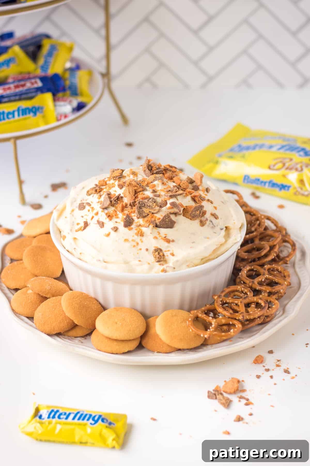 Creamy Butterfinger Fluff dessert dip served with a variety of dippers like vanilla wafers and pretzels, with Butterfinger candy bars in the background.