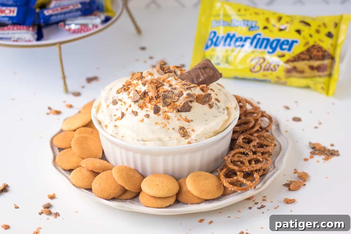 Finished Butterfinger Fluff dip, garnished with extra Butterfinger Baking Bits and a whole Butterfinger candy bar for decoration, with more baking bits in the background.