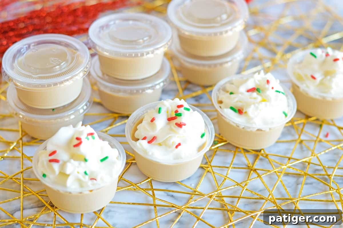 Christmas cookie jello shots with whipped cream and sprinkles lined up in a row in front of additional shots in cups with covers on them