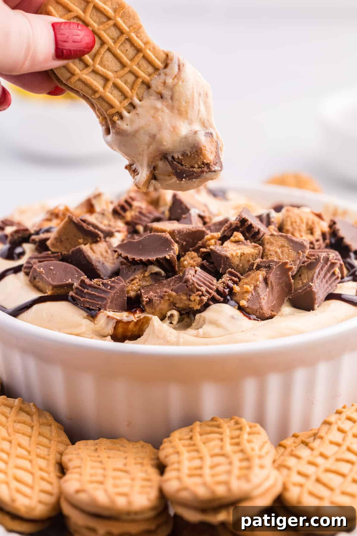 Hand reaching in and dipping Nutter Butter cookie in peanut butter cheesecake dessert dip.