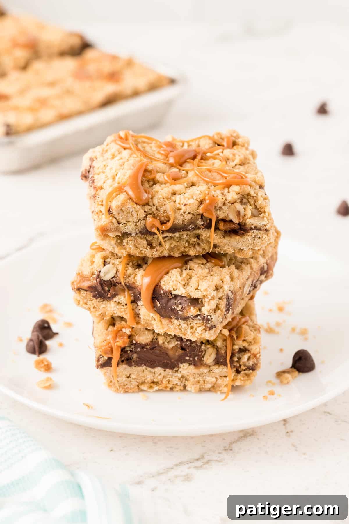Carmelitas Cookies with sticky caramel oozing out sliced into squares and stacked on top of each other on a white plate. Pan with more bars can be seen in background.