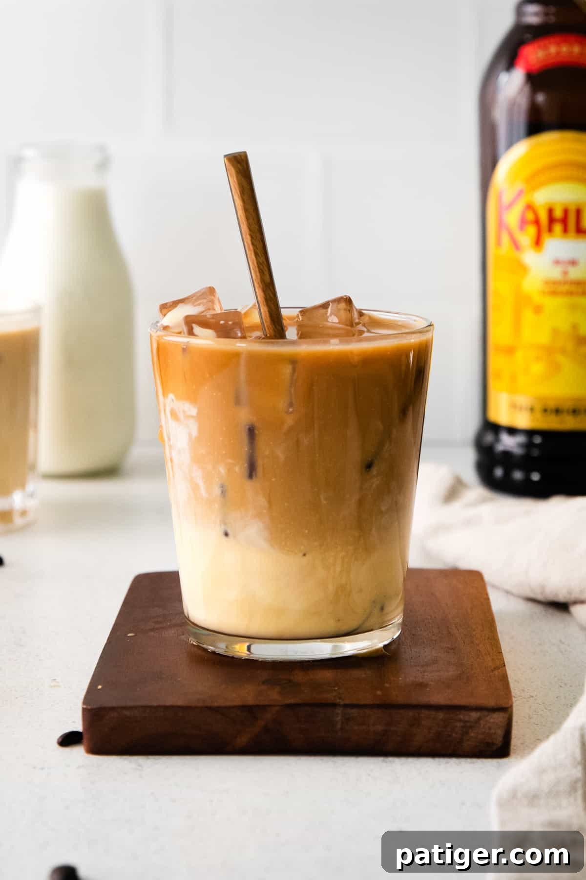 Festive Eggnog White Russian 2 A festive Eggnog White Russian cocktail in a glass with a spoon, surrounded by bottles of Kahlua, eggnog, and another holiday drink, setting a cozy winter scene.