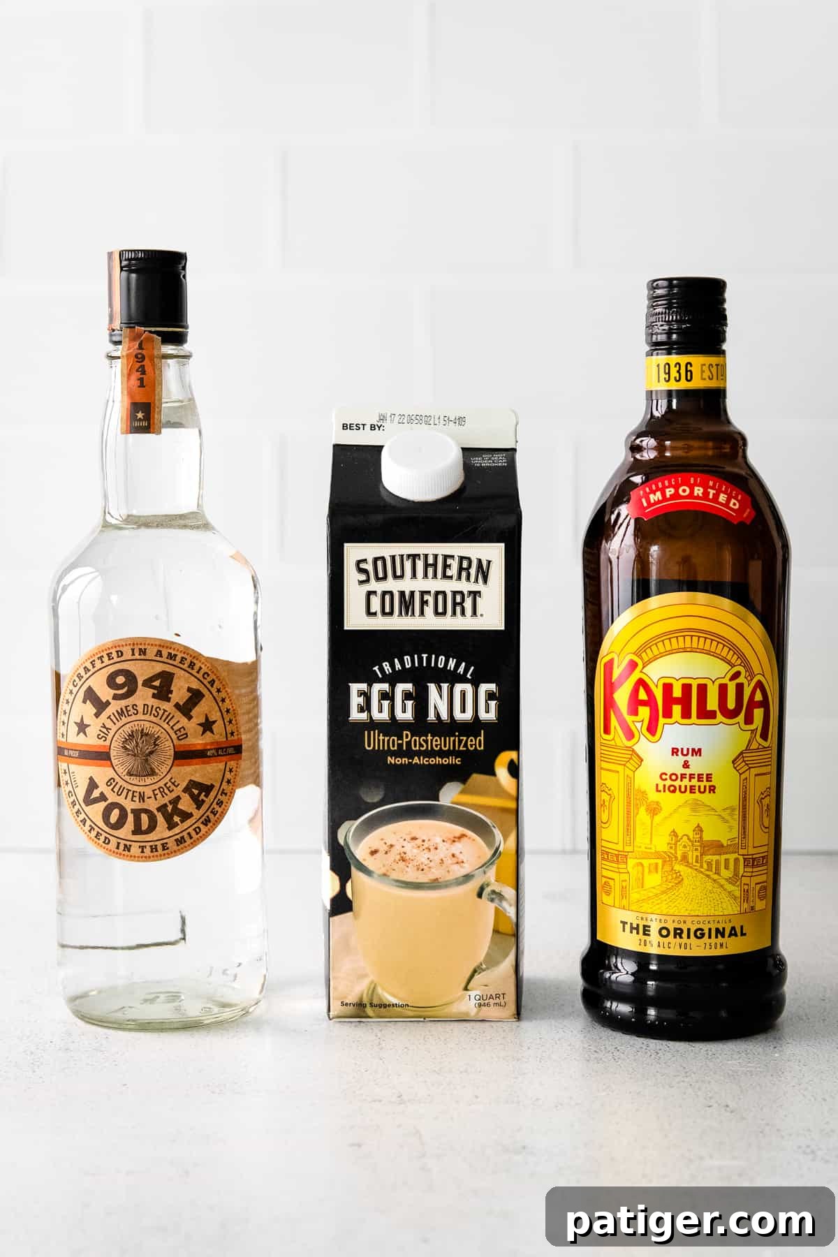 Festive Eggnog White Russian 4 A high-quality image displaying a bottle of 1941 vodka, a carton of creamy eggnog, and a bottle of Kahlua coffee liqueur, the three core ingredients for an Eggnog White Russian.