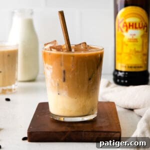 A beautiful Eggnog White Russian cocktail with a spoon in the glass, with kahlua and eggnog bottles in the background.