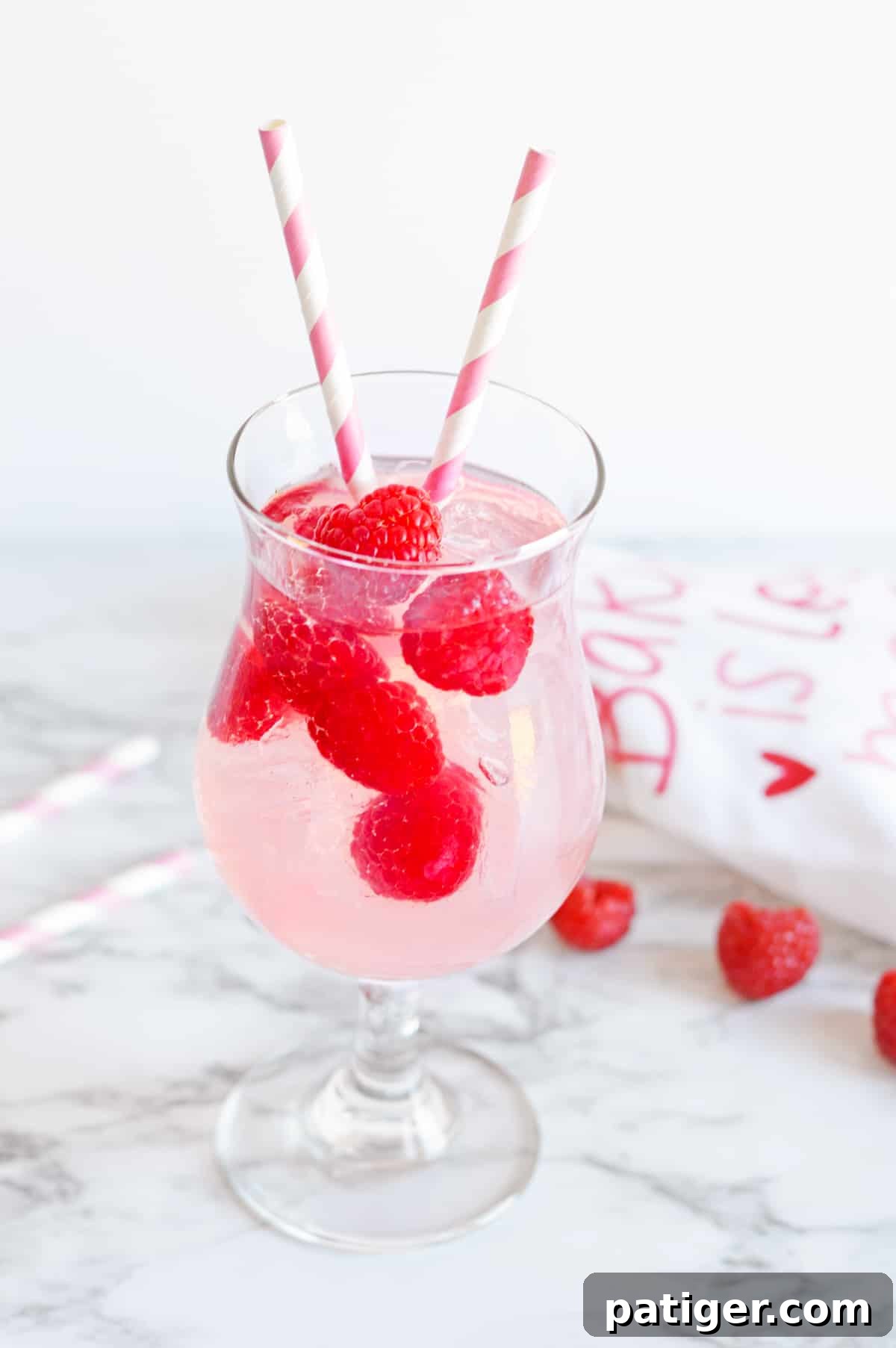 Pink Moscato Sangria with fresh raspberries in a cocktail glass with pink and white striped paper straws