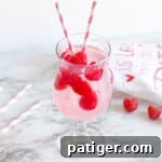 Pink Moscato Sangria with fresh raspberries in a cocktail glass with pink and white striped paper straws