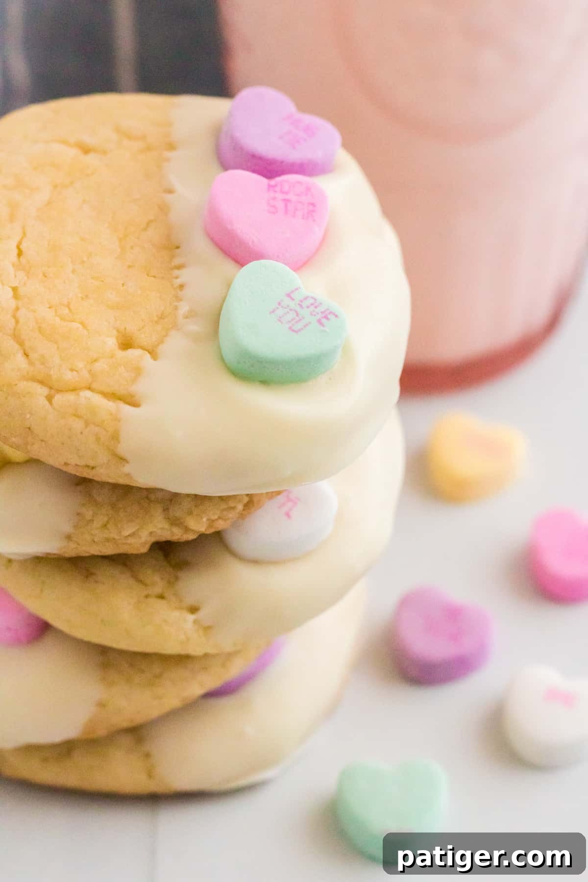 Five Valentines cake mix cookies with candy hearts stacked on top of one another with a glass of milk and more conversation heart candies around them.