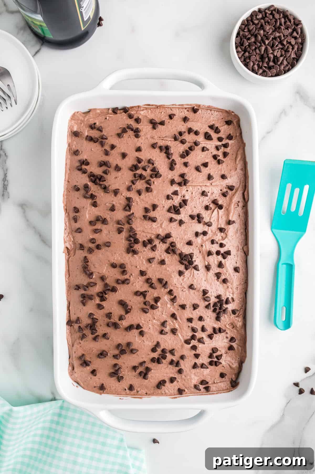 A stunning Baileys Irish cream chocolate poke cake, generously topped with an even layer of fluffy chocolate frosting and sprinkled with an abundance of mini chocolate chips, ready to be enjoyed.