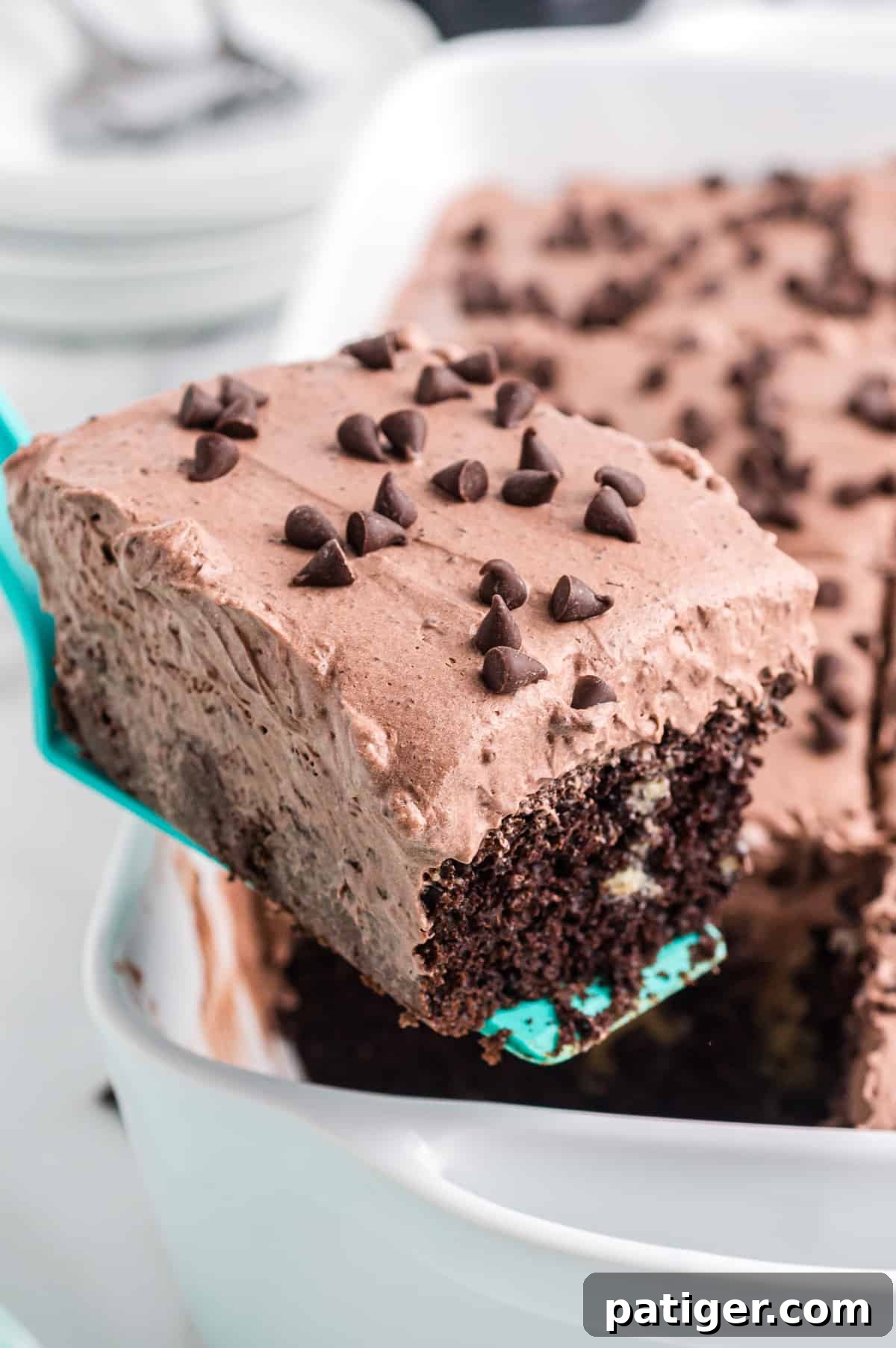 A hand serving a perfect slice of Baileys poke cake, removed cleanly from a 9x13 inch cake pan, showcasing its moist texture and layered fillings.