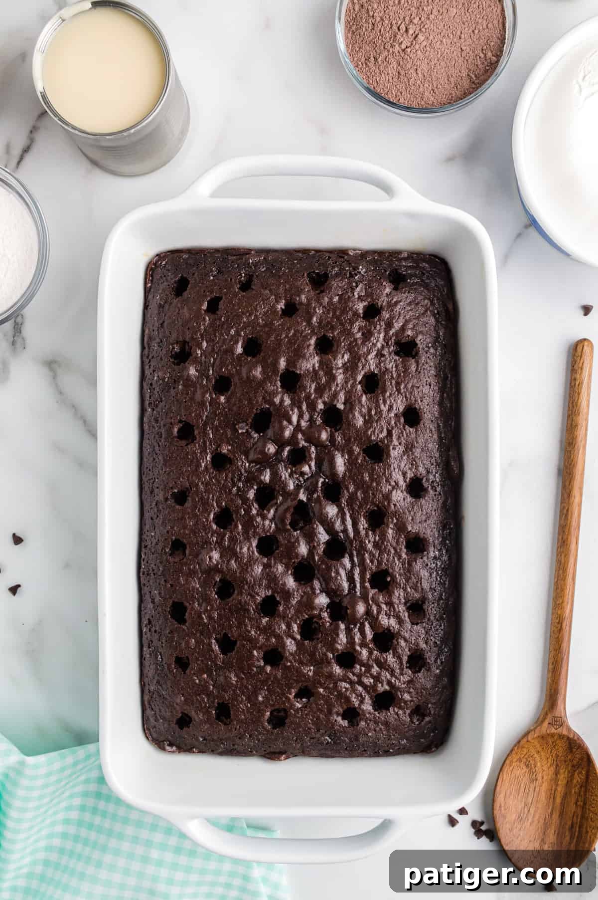 A freshly baked chocolate poke cake with numerous holes poked into its top surface using the handle of a wooden spoon, preparing it for the creamy Irish cream filling.