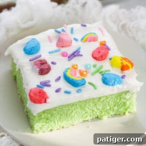 Slice of lucky charms cereal cake on white plate. The cake is bright green with white frosting topped with rainbow sprinkles and lucky charms marshmallows.