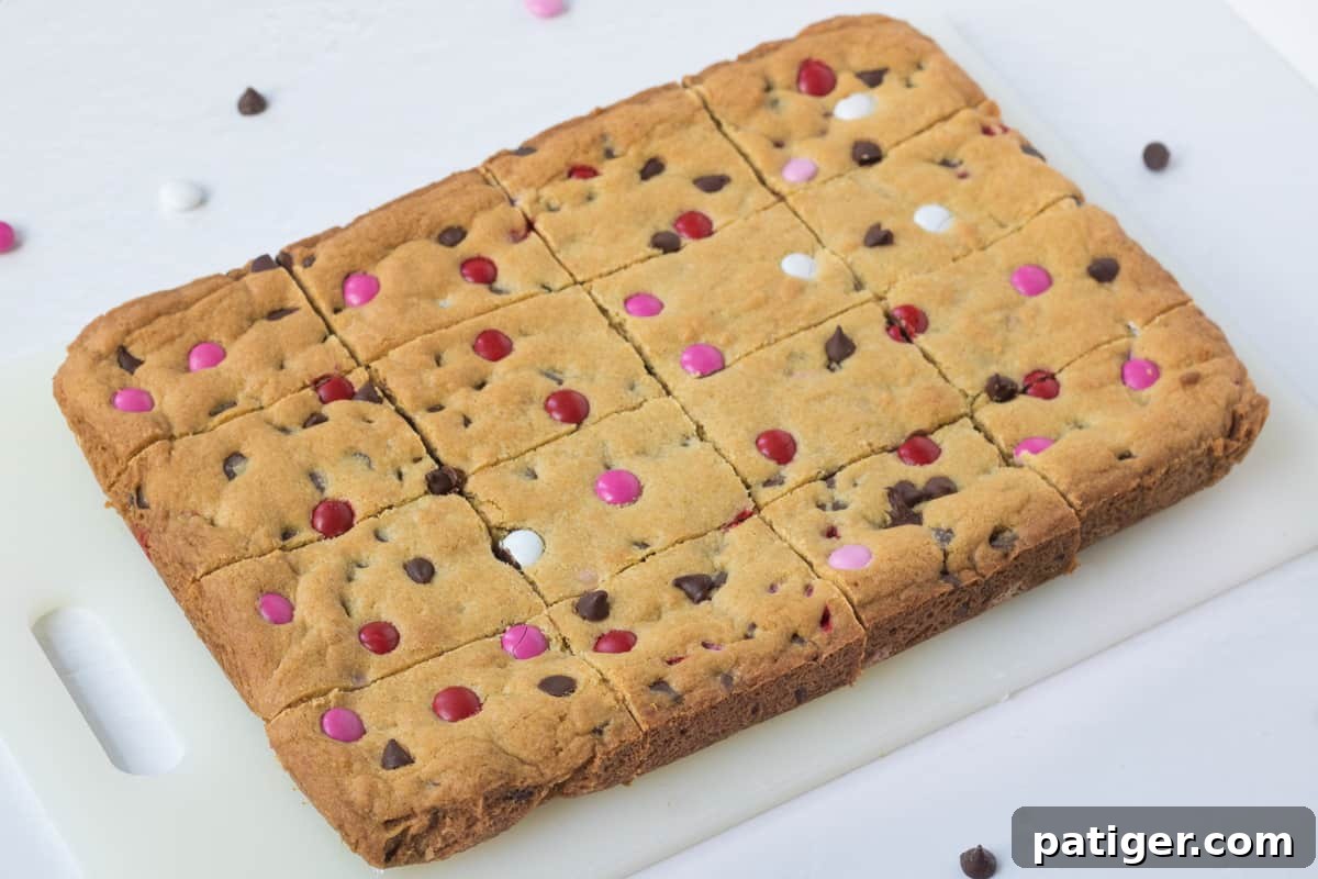 chocolate chip cookie bars with Valentine's M&M candies on a cutting board, sliced into 12 bars.