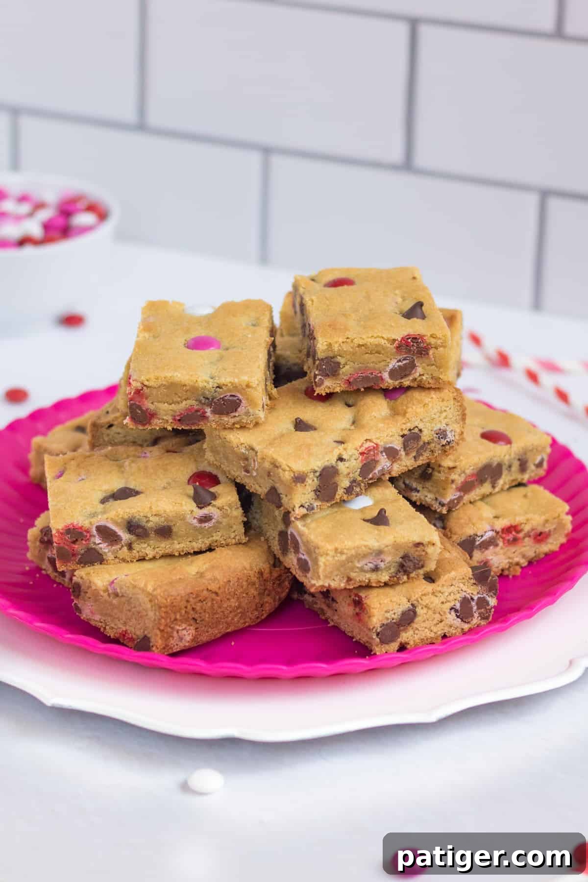 Valentines Day Cookie Bars arranged on a pink serving platter with red and pink paper straws and M&M candies around them.