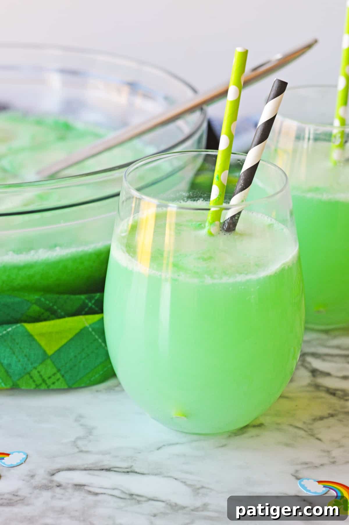 Clover Kick 2 Shamrock Punch in a stemless wine glass with another glass of the green punch and punch bowl in the background.