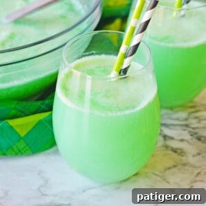 Clover Kick 7 Shamrock Punch in a stemless wine glass with another glass of the green punch and punch bowl in the background.