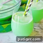 Clover Kick 8 Shamrock Punch in a stemless wine glass with another glass of the green punch and punch bowl in the background.