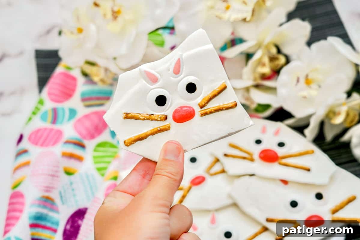 A hand holding a piece of Easter bark, showcasing a finished bunny face made from pretzels, jelly beans, candy ears, and candy eyes, ready to be enjoyed as a festive treat.