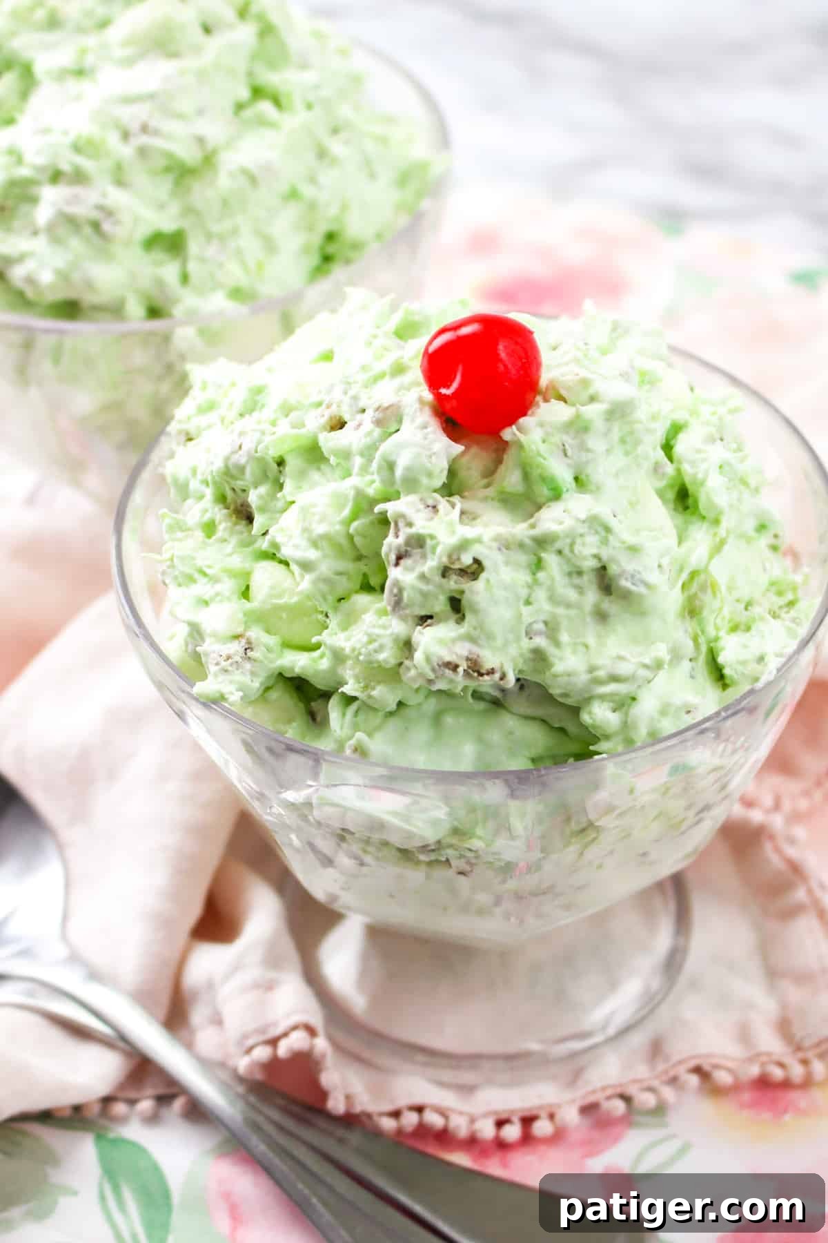 Watergate salad in a elegant serving glass, garnished with a vibrant red cherry on top, highlighting its creamy green texture.
