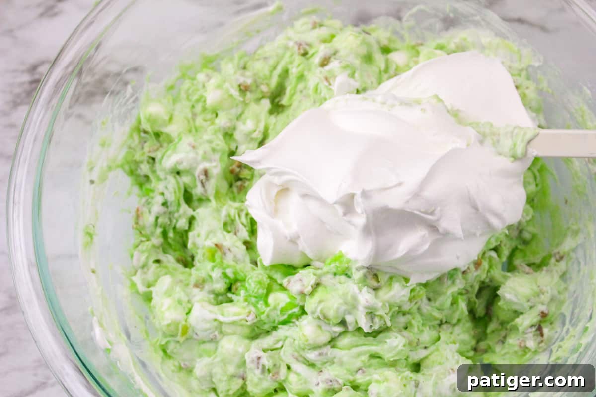 The pistachio salad mixture with a generous dollop of Cool Whip on top, ready to be folded in to create a creamy and fluffy dessert.