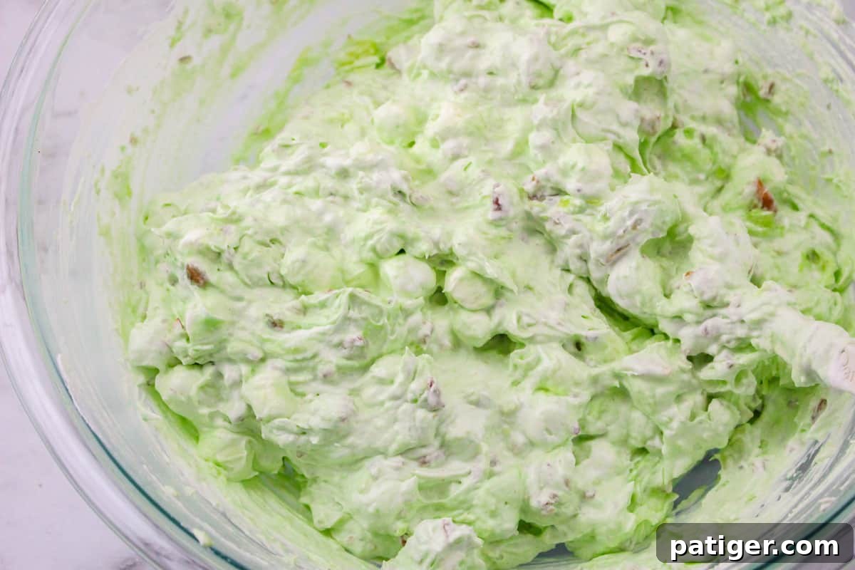 A large glass bowl filled with the finished pistachio delight dessert salad, showcasing its fluffy green texture and the visible pieces of pineapple and pecans, ready for serving.