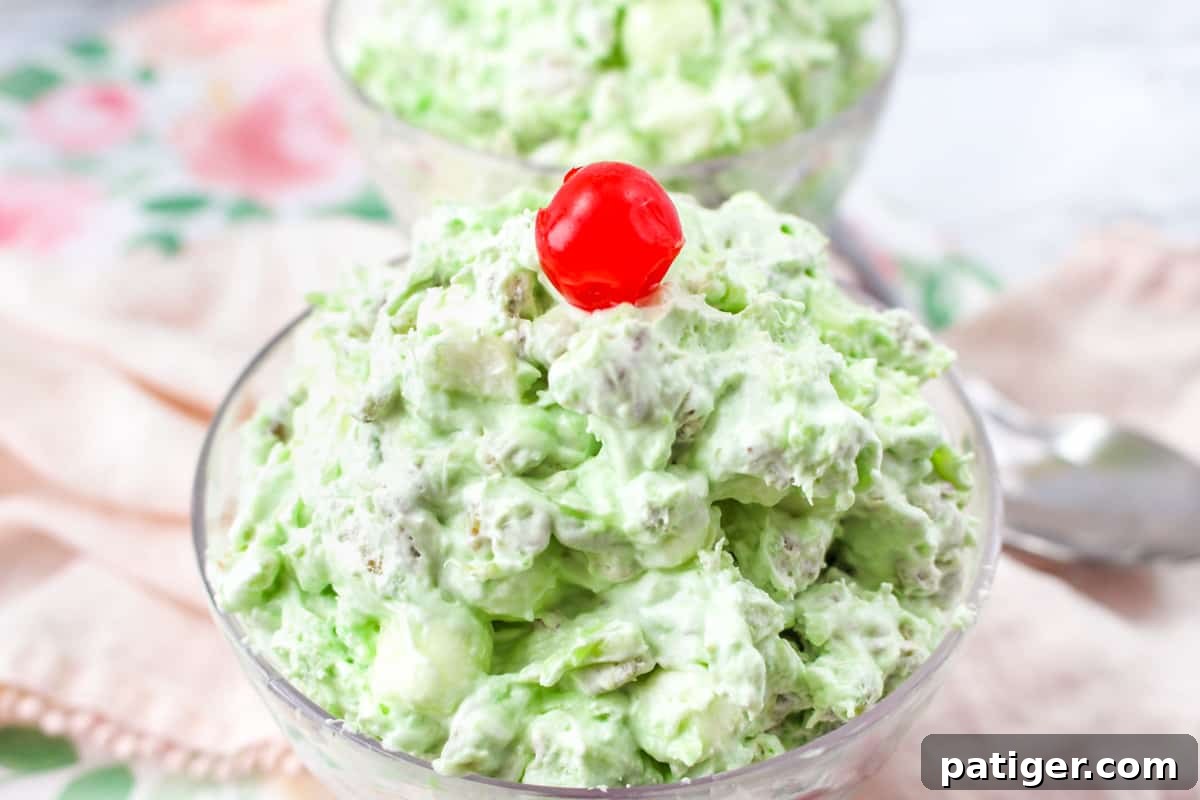 Close-up of Watergate Salad in a glass bowl, featuring its vibrant green color, fluffy texture, visible pecans, and a maraschino cherry garnish, ready for serving or storage.