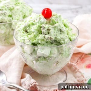 Watergate salad in a glass bowl topped with a cherry.