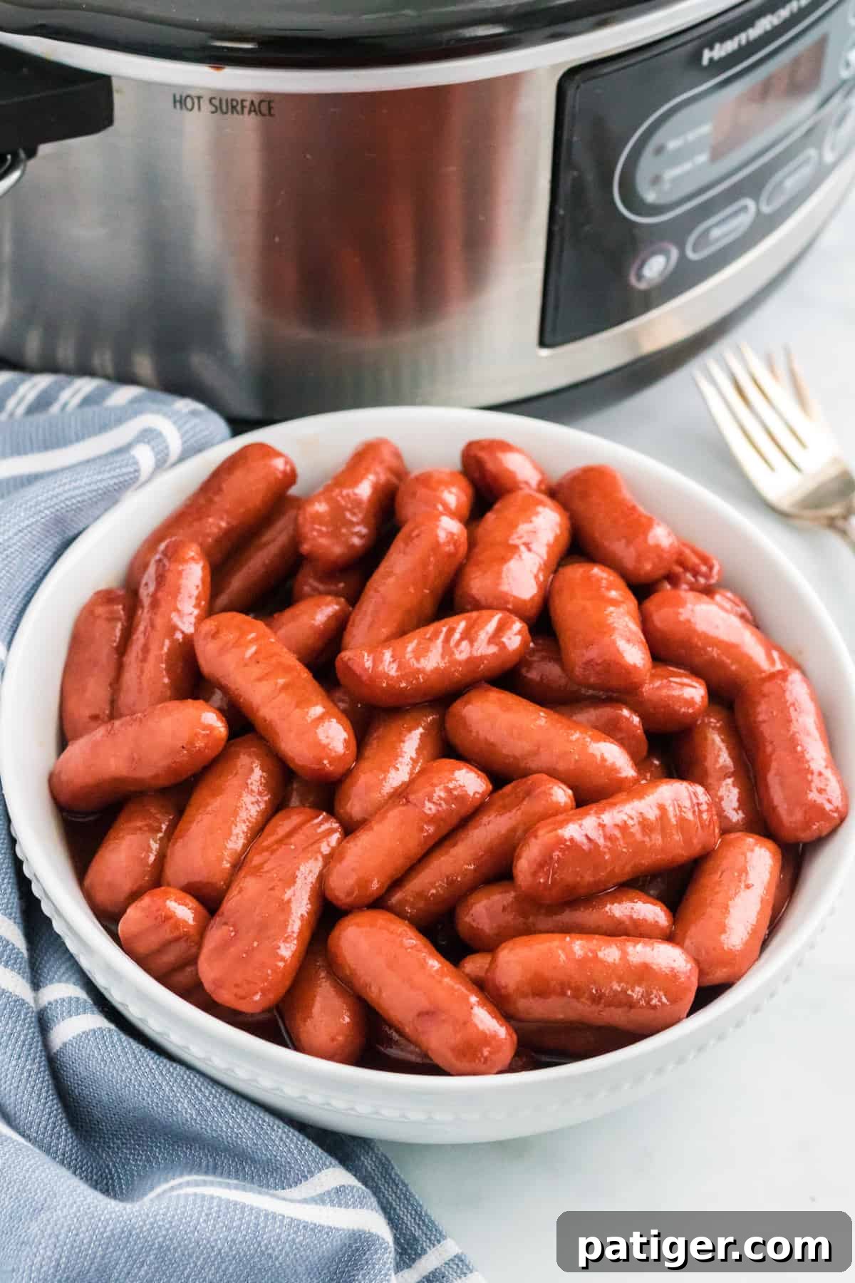 Sweet Glazed Slow Cooker Smokies 2 Crockpot little smokies with barbecue sauce and grape jelly in a white bowl with slow cooker in the background.