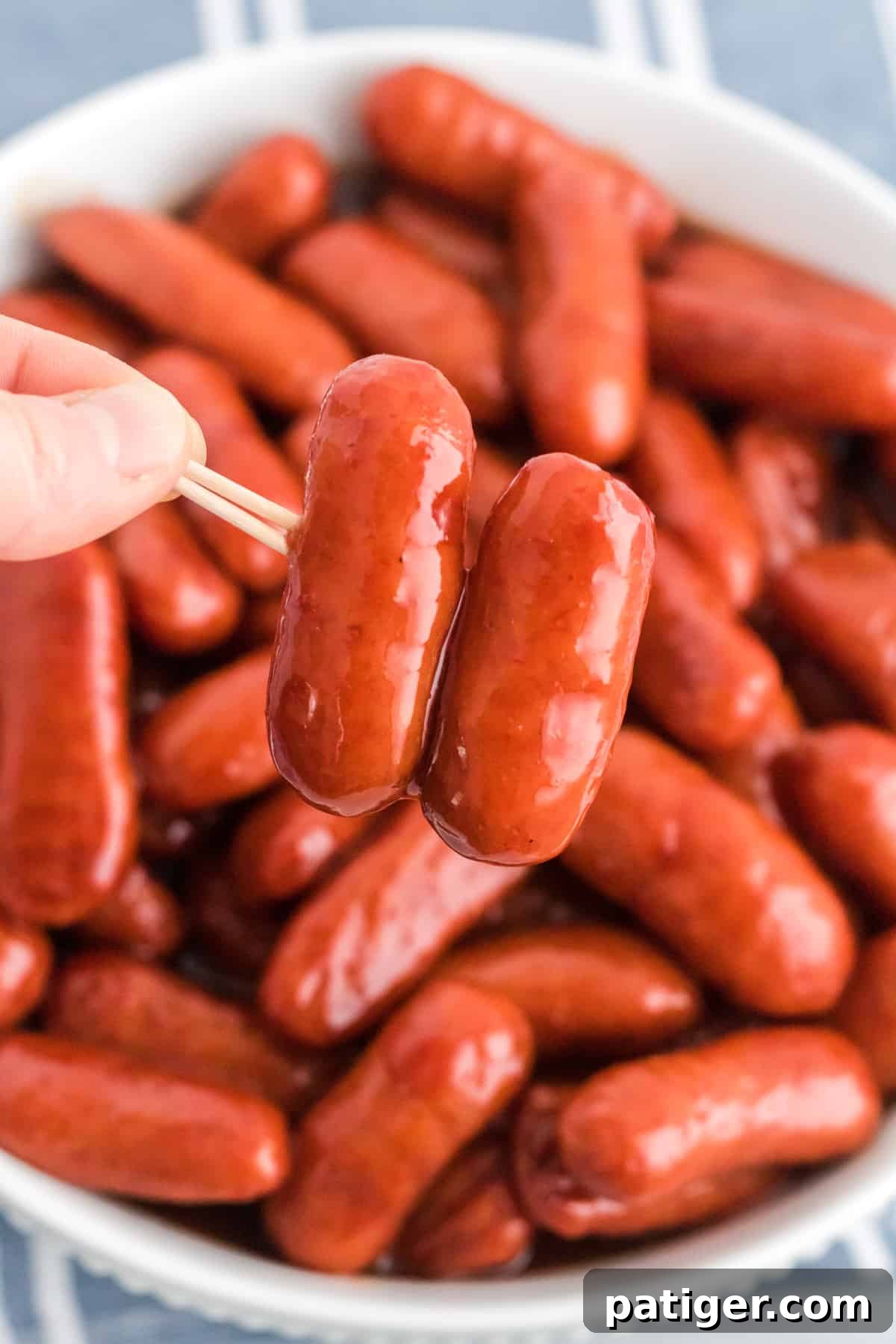 Sweet Glazed Slow Cooker Smokies 7 Two cocktail weenies on a toothpick with rest of slow cooker lil smokies in a bowl in the background.
