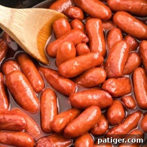 Little Smokies Cocktail Sausages in a slow cooker with a wooden spoon.