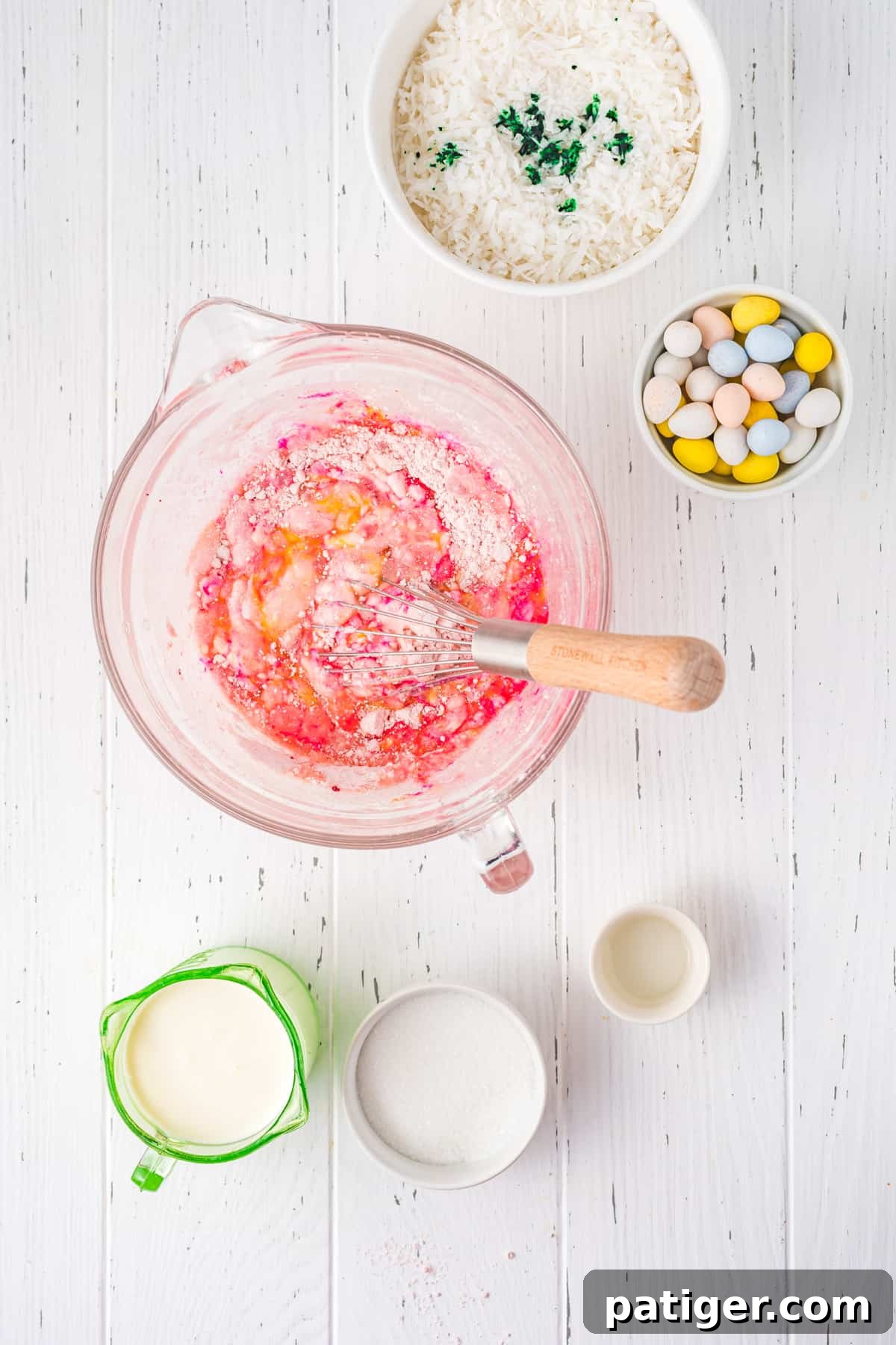 Mixing bright pink strawberry cake batter in a large clear glass bowl using an electric hand mixer.