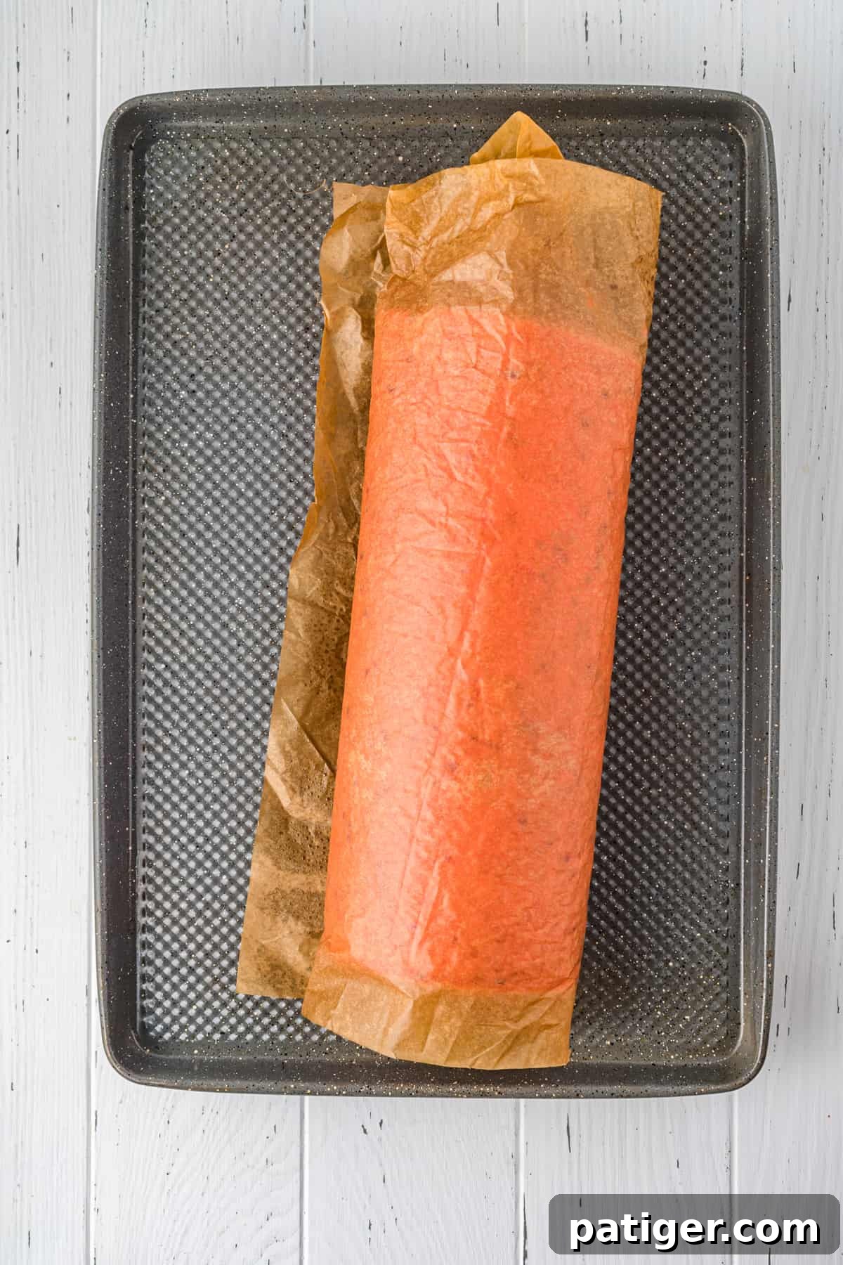 A warm, freshly baked strawberry cake still rolled up in parchment paper, resting on a jelly roll pan to cool.