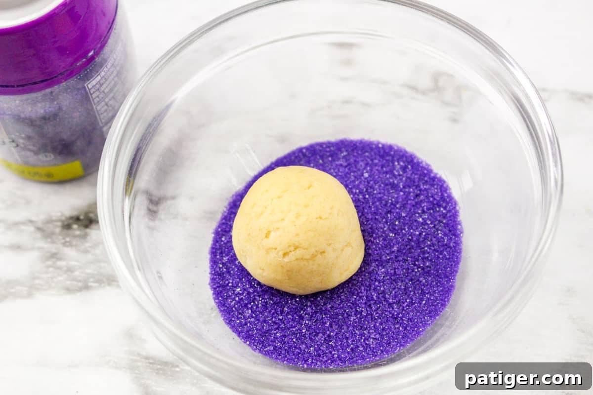 Spring Blossom Delights 6 A hand gently rolls a ball of cookie dough in vibrant pink colored sugar, preparing it for baking and creating the festive Easter blossom effect.