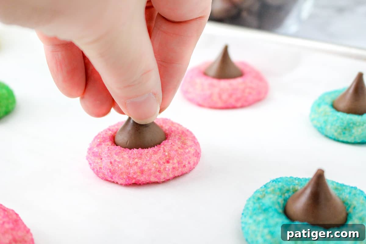 Spring Blossom Delights 8 A hand gently presses a silver-foiled Hershey's Kiss into the warm center of a freshly baked pink sugar cookie, creating the iconic blossom shape.